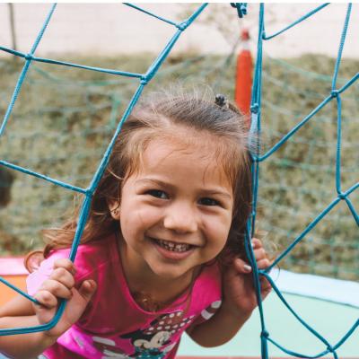 Young child peeking through a net or fence and smiling